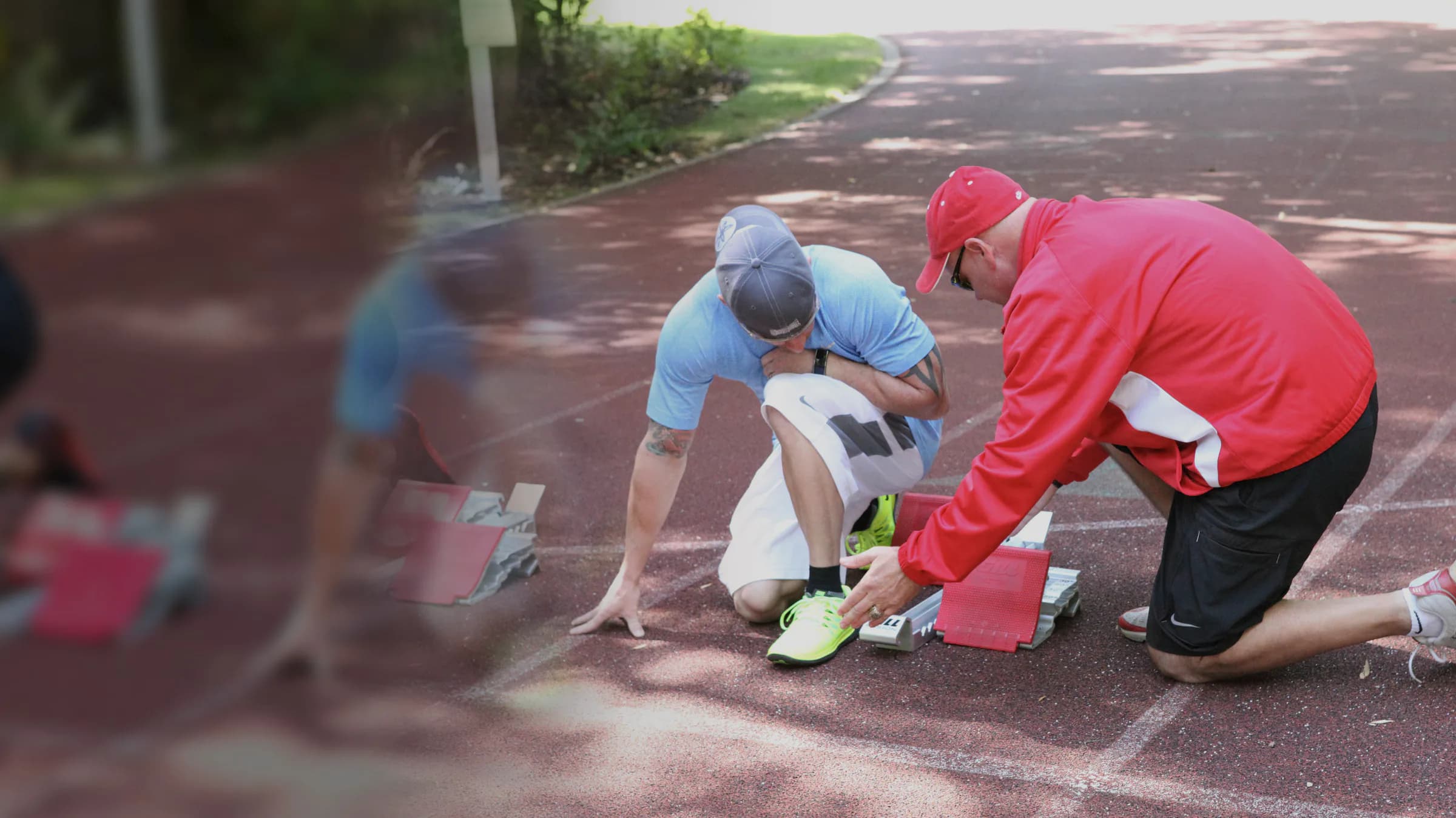 A coach guides a sprinter beside the starting blocks